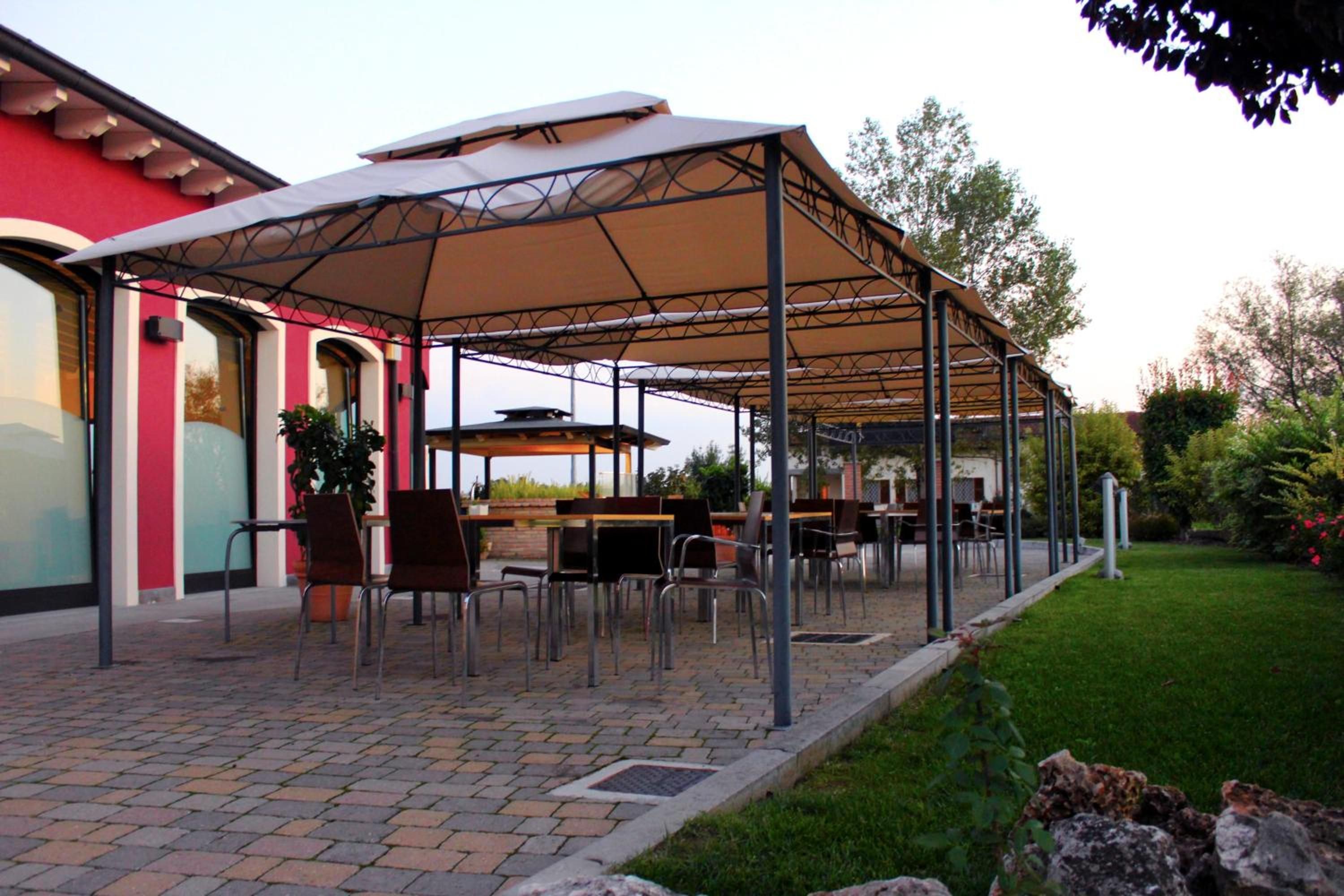Un patio al aire libre con mesas y sillas, una zona cubierta con techo y un sendero de ladrillo.