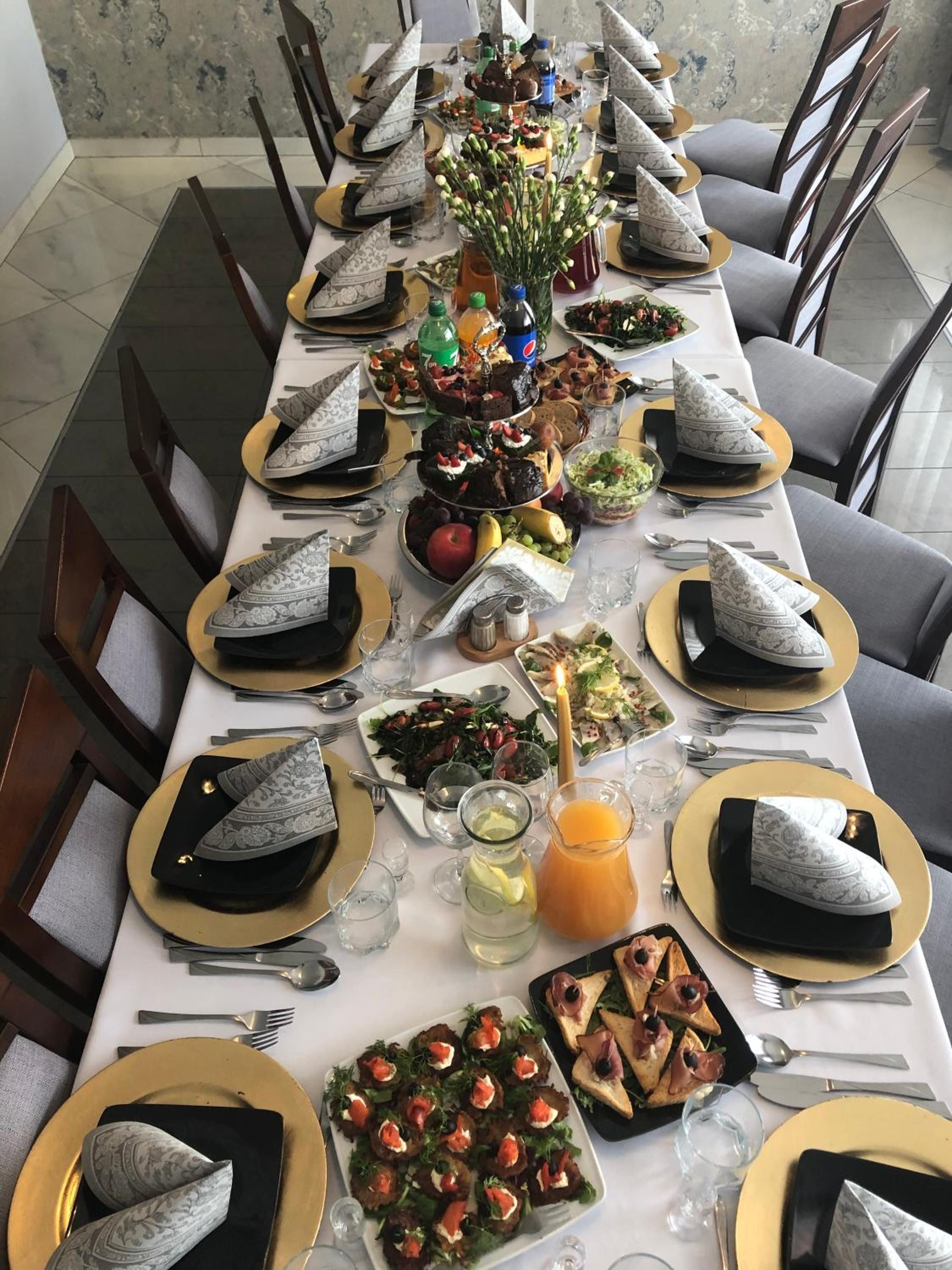 A long dining table set with multiple dishes, including salads, appetizers, and a centerpiece with flowers.