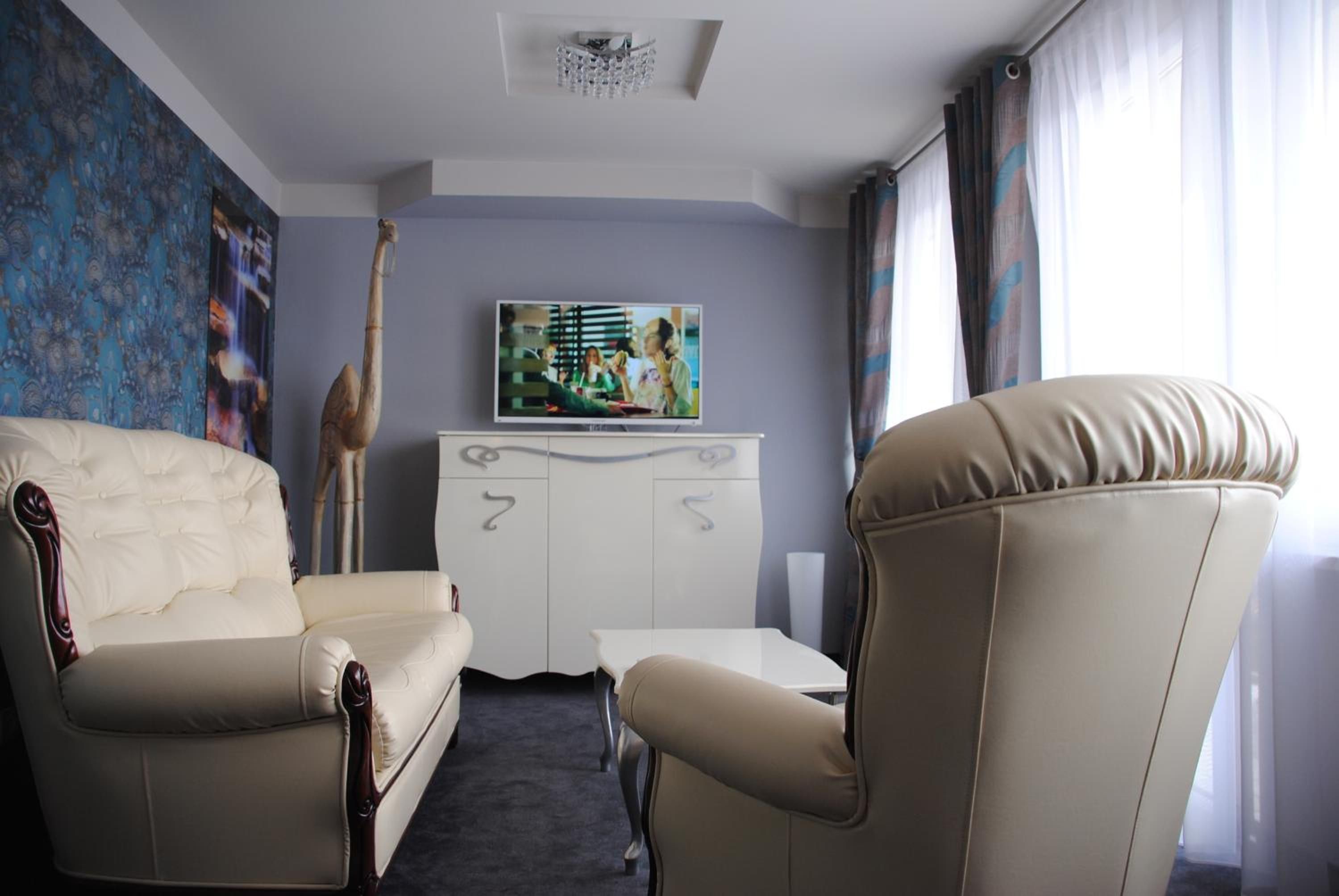 A hotel room with a sofa, armchair, television, and a painting on the wall.