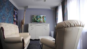 A hotel room with a sofa, armchair, television, and a painting on the wall.