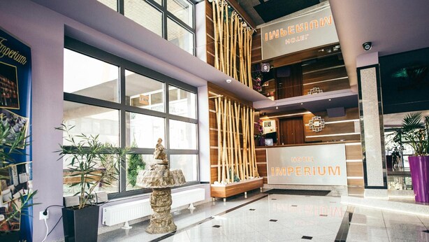 A hotel lobby with a reception desk, large windows, and a decorative rock sculpture. - Hotel Imperium (Pionki)