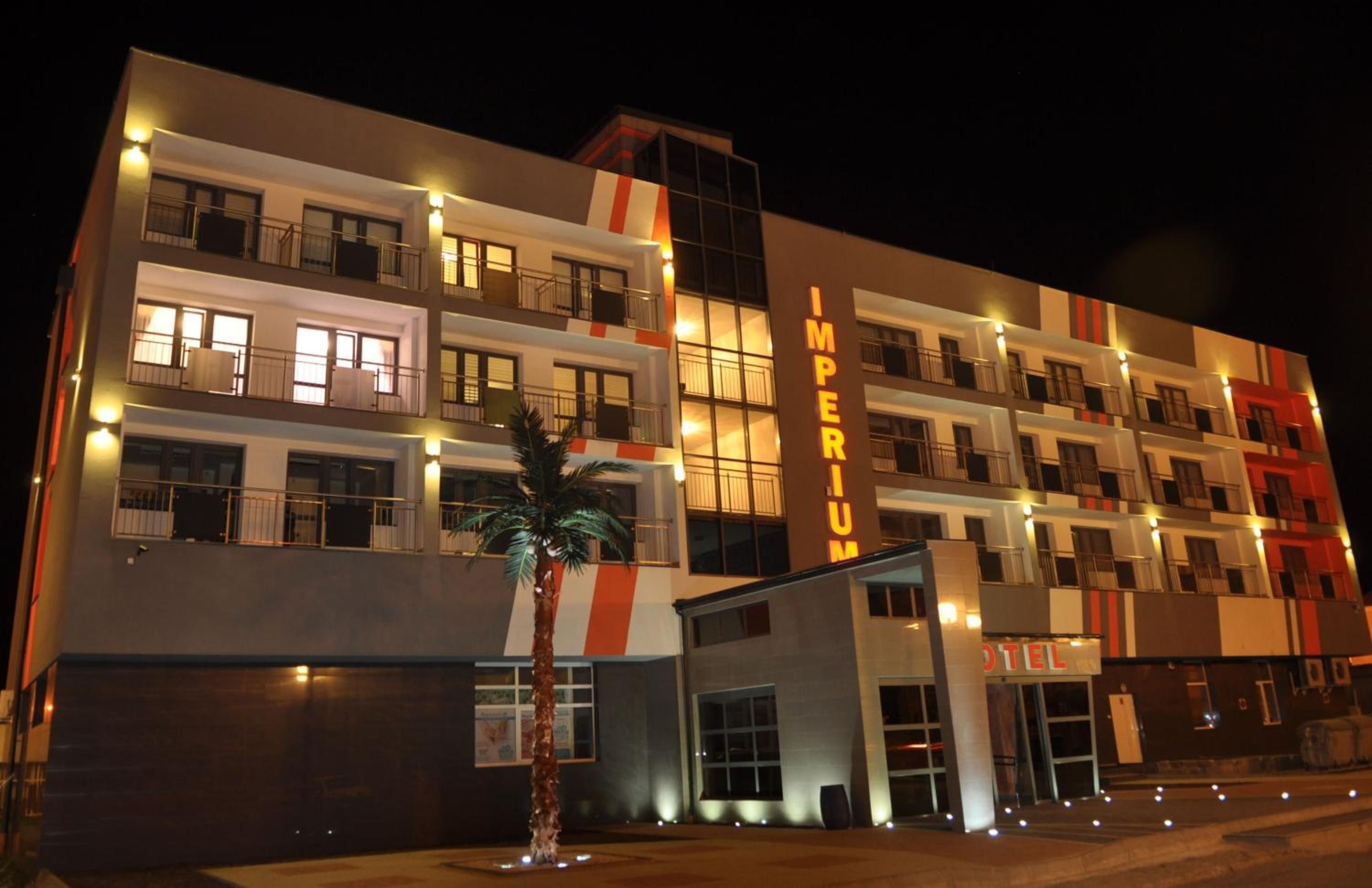A multi-story hotel with a modern facade, illuminated windows, and a prominent 'IMPERIUM' sign.