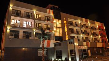 A multi-story hotel with a modern facade, illuminated windows, and a prominent 'IMPERIUM' sign.