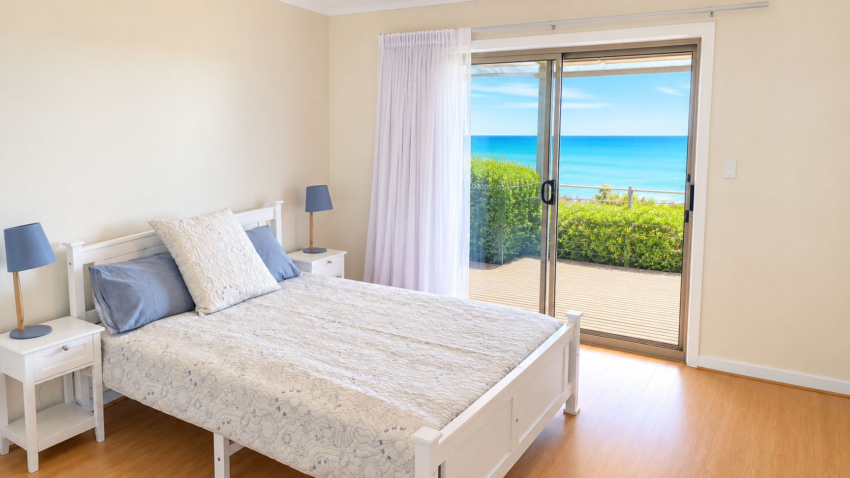A bedroom with a bed, nightstands, a window with a view of the sea, and a sliding glass door.