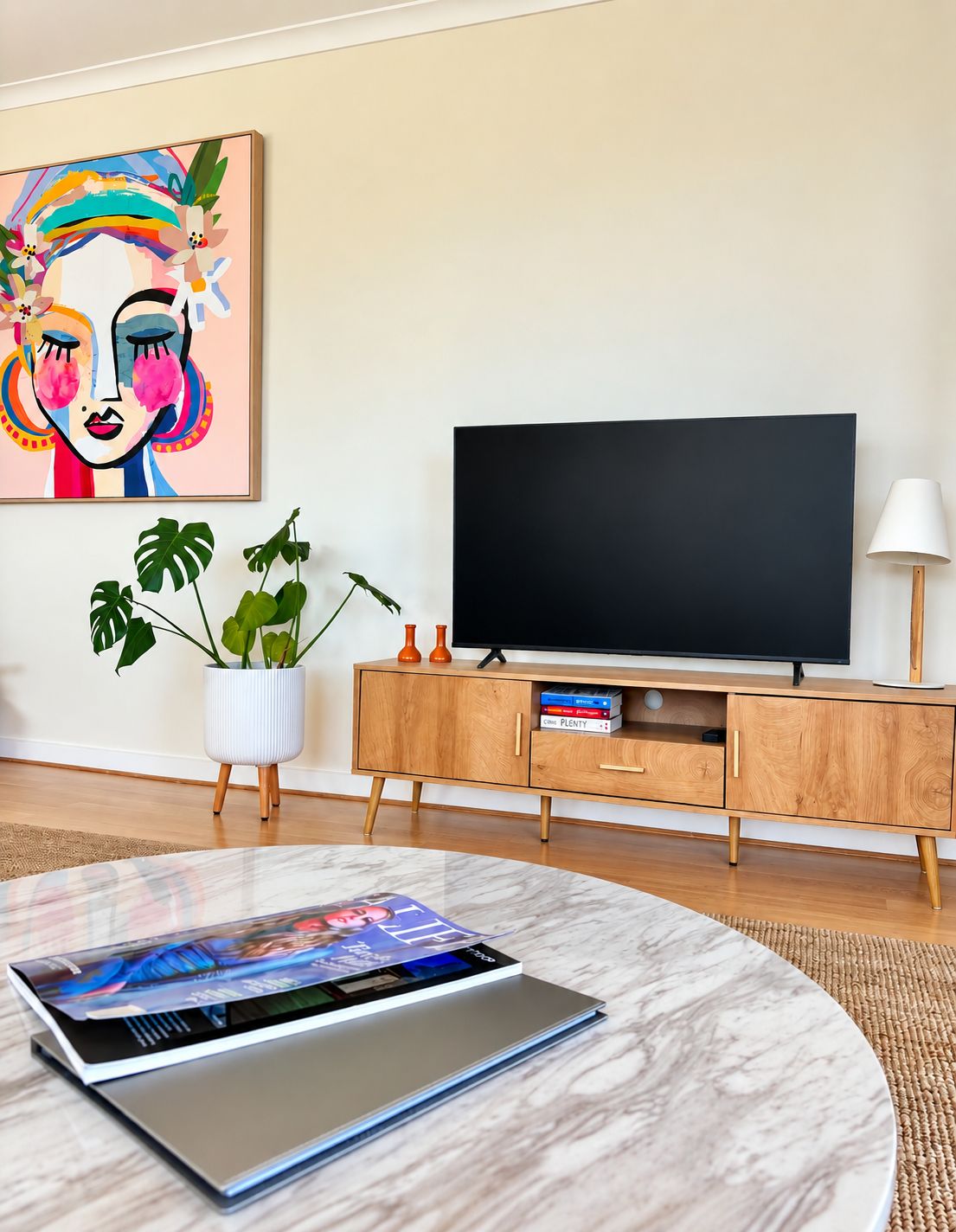 A modern living room with a flat-screen TV, a wooden cabinet, a potted plant, and a magazine on a marble table.