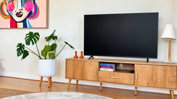 A modern living room with a flat-screen TV, a wooden cabinet, a potted plant, and a magazine on a marble table.