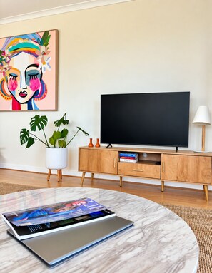 A modern living room with a flat-screen TV, a wooden cabinet, a potted plant, and a magazine on a marble table.