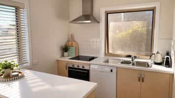 A kitchen with a dishwasher, stove, sink, and a window with frosted glass.