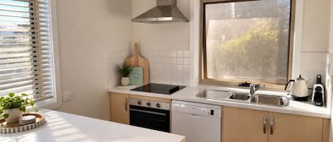 A kitchen with a dishwasher, stove, sink, and a window with frosted glass.