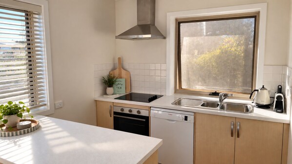 A kitchen with a dishwasher, stove, sink, and a window with frosted glass.