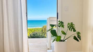 Une chambre avec un lit, une plante en pot et une vue sur l’océan, visible à travers une porte coulissante.