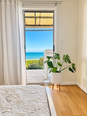 A bedroom with a bed, a potted plant, and a view of the ocean through a sliding door.