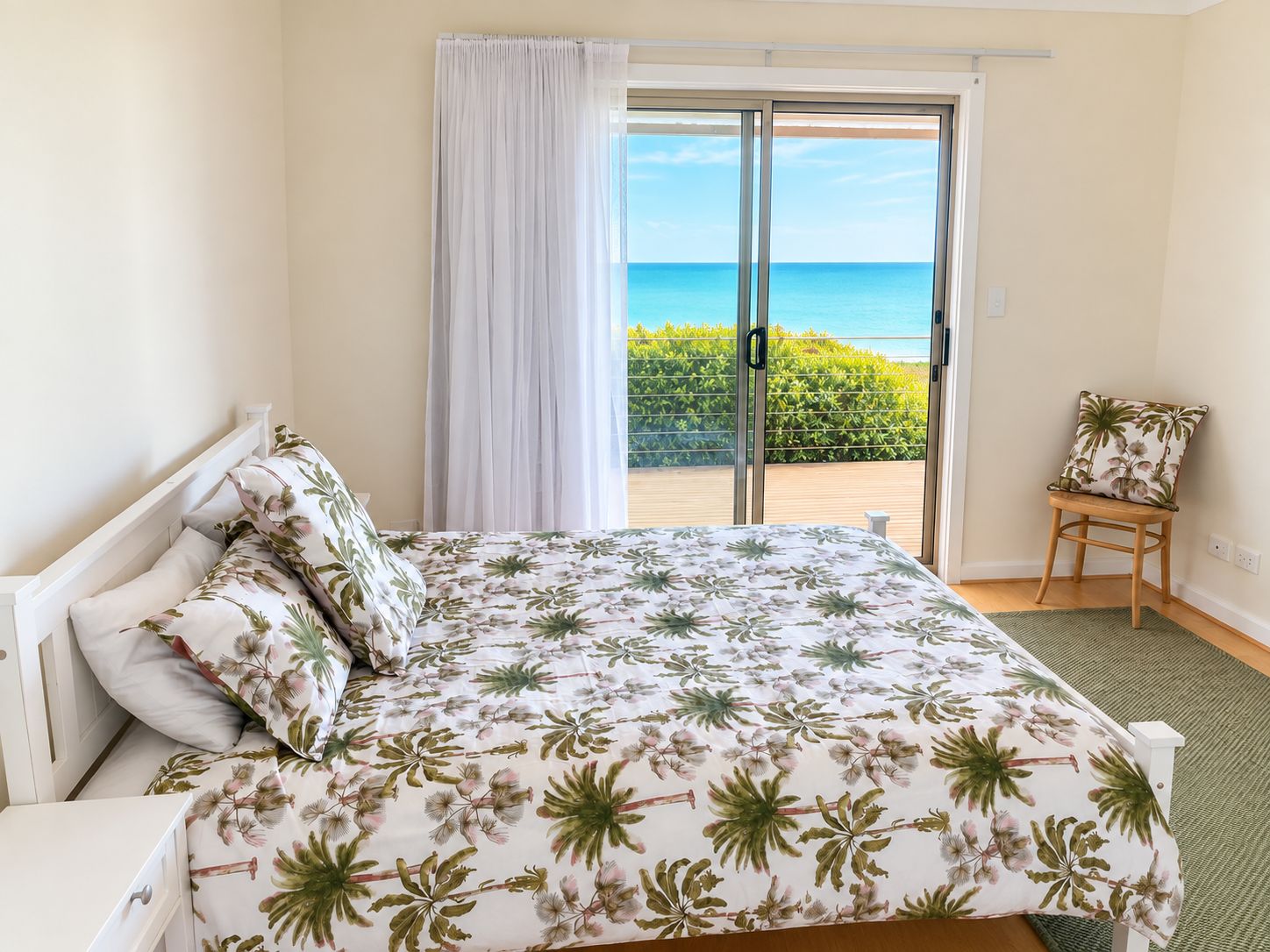A bedroom with a bed, a chair, a view of the sea, and a balcony.