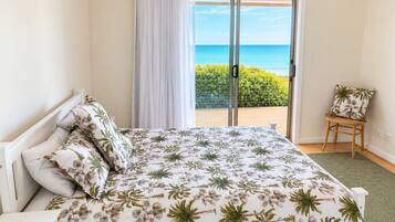 A bedroom with a bed, a chair, a view of the sea, and a balcony.
