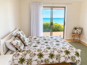 A bedroom with a bed, a chair, a view of the sea, and a balcony.