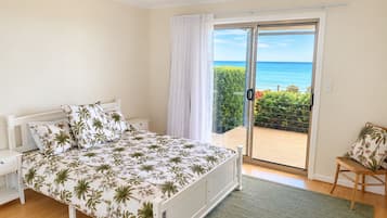 Une chambre à coucher comprenant un lit, une table de chevet, une chaise et une vue sur la mer, accessible par une porte-fenêtre coulissante.