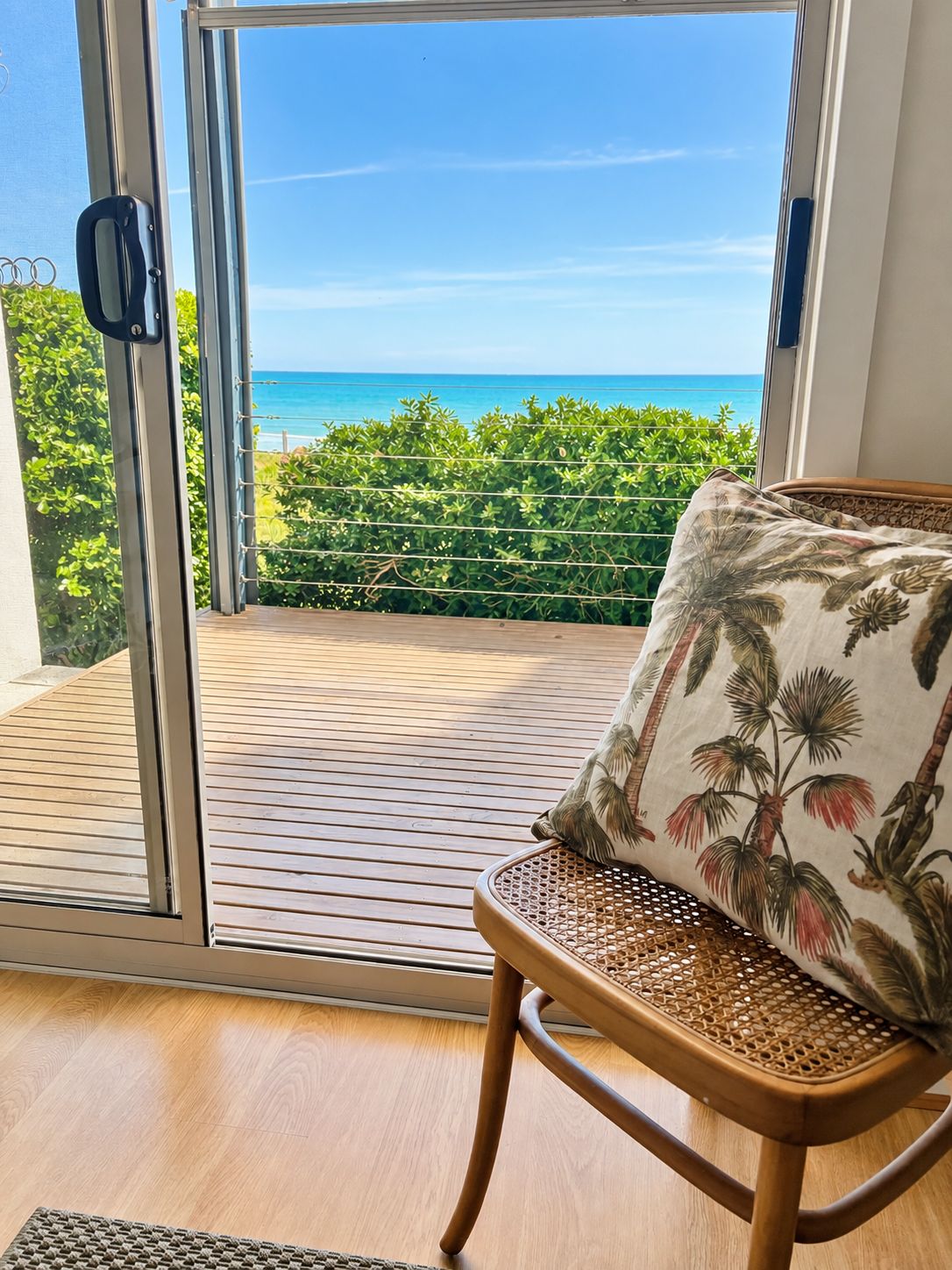 A room with a view of the ocean, a wicker chair with a floral cushion, and a wooden floor.