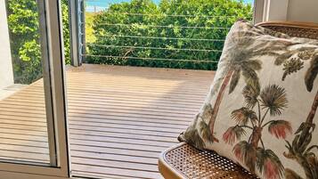 A room with a view of the ocean, a wicker chair with a floral cushion, and a wooden floor.