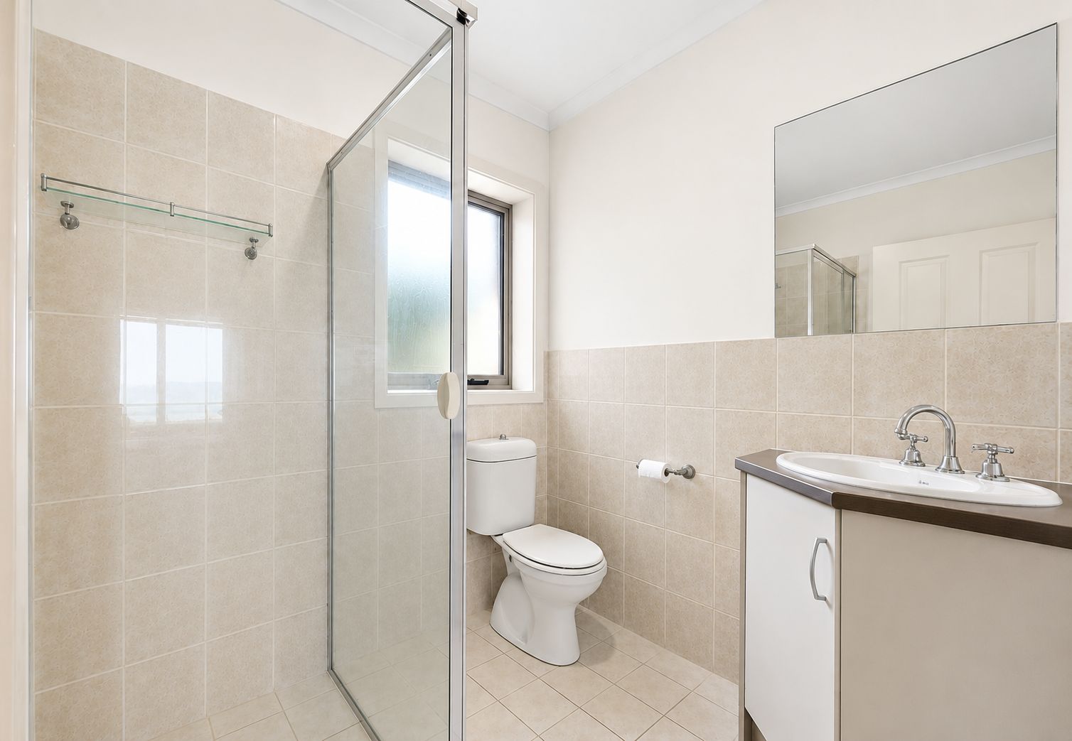 Ein modernes Badezimmer mit Duschkabine aus Glas, Toilette und Waschbecken mit Spiegel darüber.