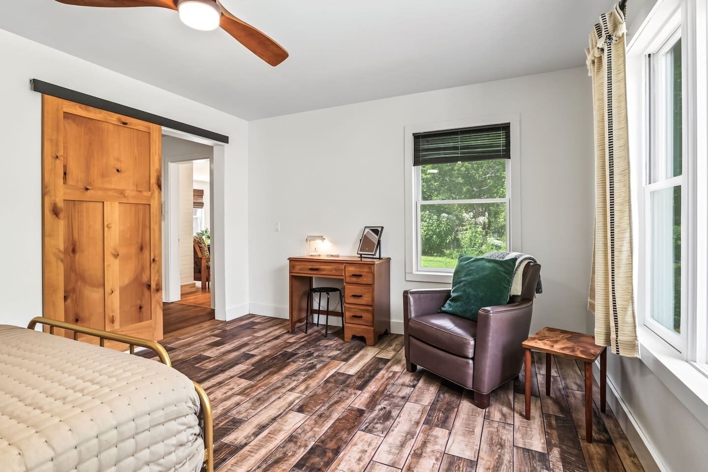 A bedroom with a bed, a desk, a chair, a wardrobe, and a window with a view of greenery.