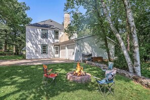 A two-story house with a garage, a fire pit with chairs, and a well-maintained lawn.