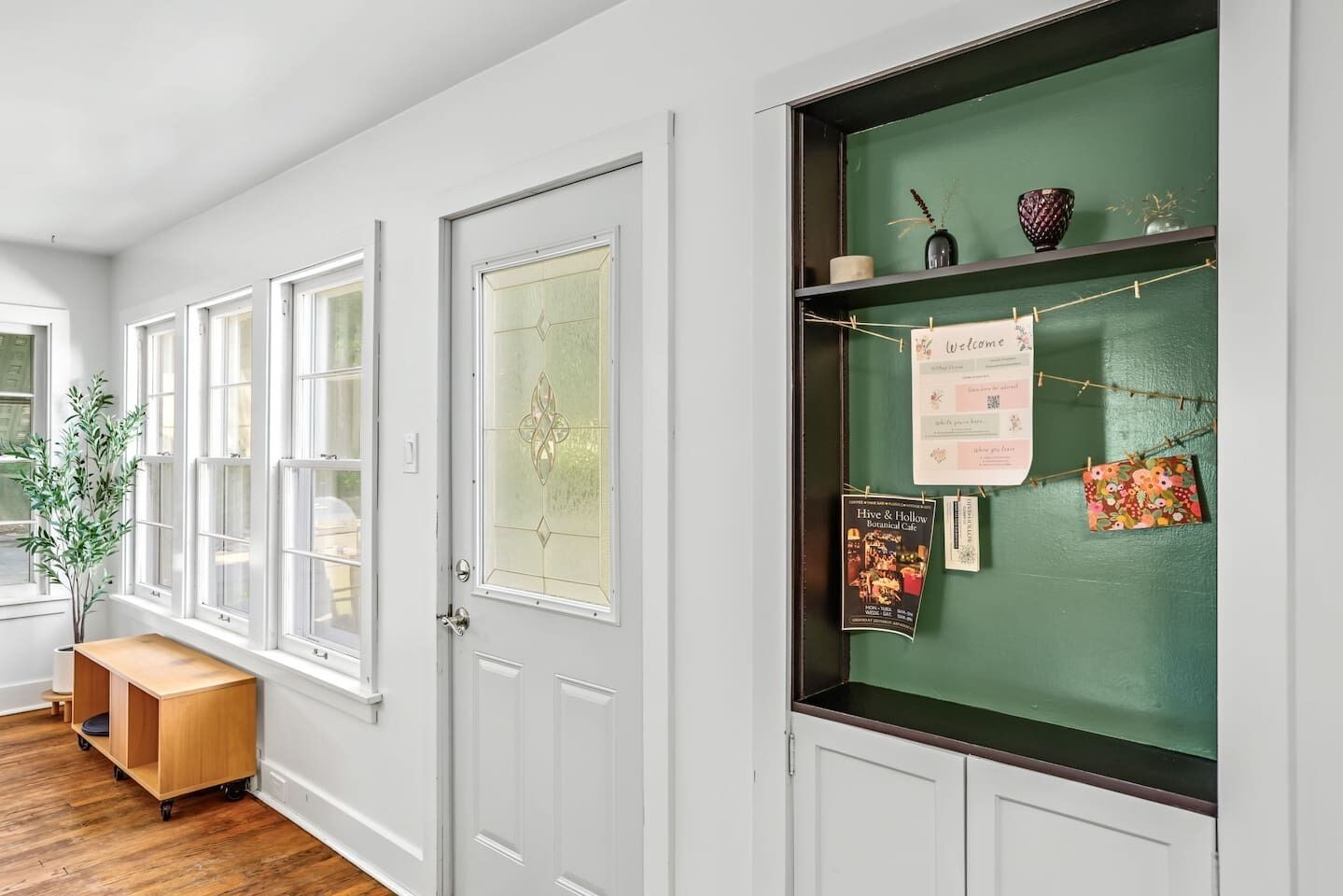 A room with white doors, a green bulletin board with notes, and a wooden bench.