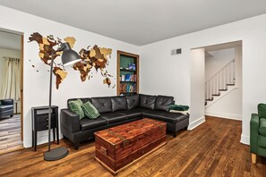 A modern living room with a sectional sofa, a wooden coffee table, a world map wall art, a bookshelf, and a staircase.