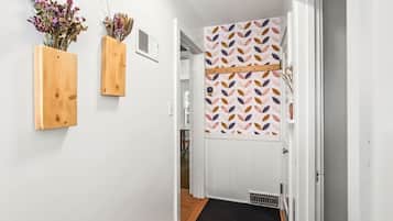 Un pasillo con una puerta de madera, un felpudo negro en la entrada y dos macetas de madera fijadas a la pared con flores secas.