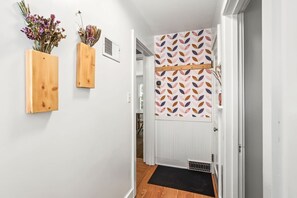A hallway with a wooden door, a black mat at the entrance, and two wooden wall-mounted planters with dried flowers.