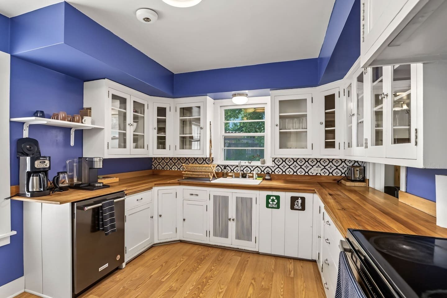 A modern kitchen with white cabinets, a wooden countertop, a dishwasher, and a stove.