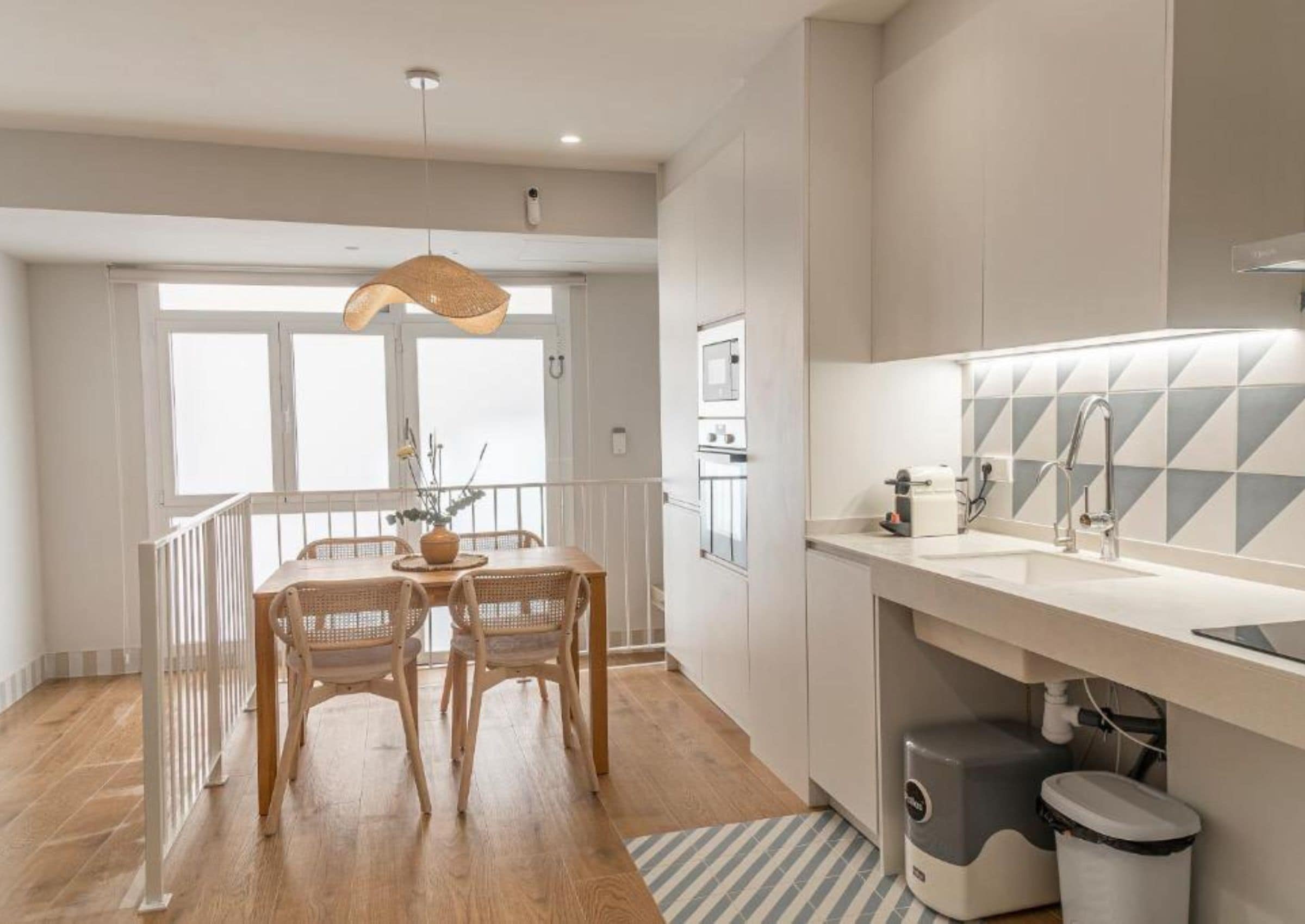 A modern kitchen with a dining area, wooden flooring, and a view of the outdoors.