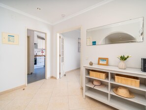 A hallway with a kitchen area visible through an open door, a white console table with storage baskets, and a large mirror on the wall. - Spacious Stylish Apartment near Lagos Centre (Lagos)