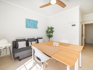 Ein modernes Wohnzimmer mit einem Holzesstisch, einem grauen Sofa und einem Deckenventilator.