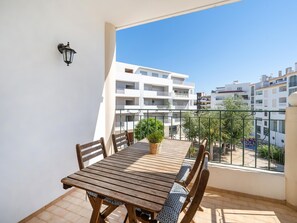 Ein Balkon mit Holztisch und -stühlen, einem Blumentopf und Blick auf die umliegenden Gebäude.