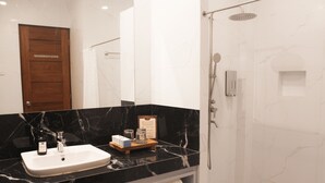 A modern bathroom with a marble sink, a glass shower enclosure, and a wooden door. - Port Royale Waterpark Resort Tacloban (Tacloban)