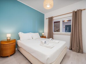 Habitación de hotel con una cama grande, dos mesitas de noche, una ventana con cortinas y una lámpara colgante.