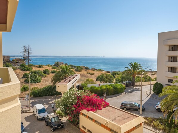 Zona residencial costera con vista al mar, coches aparcados y un edificio con balcón.