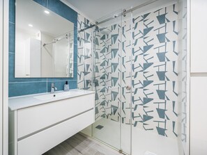 Un baño con tocador blanco, espejo, ducha con diseño de baldosas geométricas y pared de acento azul.