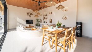 Una sala de estar moderna con techo de madera, un comedor con mesa y sillas, y un televisor de pantalla plana montado en la pared.