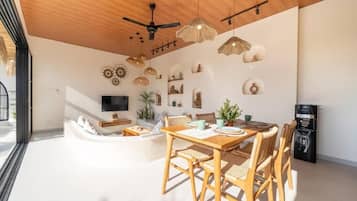 Un salon moderne avec un plafond en bois, un coin repas comprenant une table et des chaises, et un téléviseur à écran plat fixé au mur.