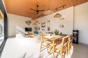 A modern living room with a wooden ceiling, a dining area with a table and chairs, and a flat-screen TV mounted on the wall. - Disenta Villa (Badung)