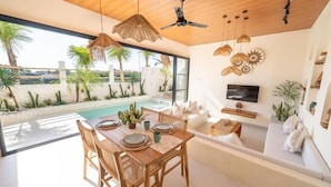 A modern interior with a dining area, a pool, and a living space with a TV. - Disenta Villa (Badung)