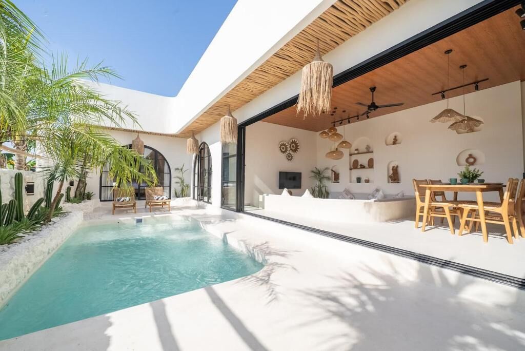 A modern outdoor pool area with a clear blue pool, surrounded by white walls and wooden furniture.