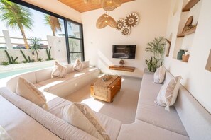 A modern living room with a large sofa, a coffee table, and a TV mounted on the wall. - Disenta Villa (Badung)