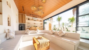 A modern living room with a large sofa, a wooden coffee table, and a kitchen area with a refrigerator. - Disenta Villa (Badung)