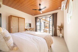 A bedroom with a bed, a ceiling fan, a desk, and a view of the outside. - Disenta Villa (Badung)