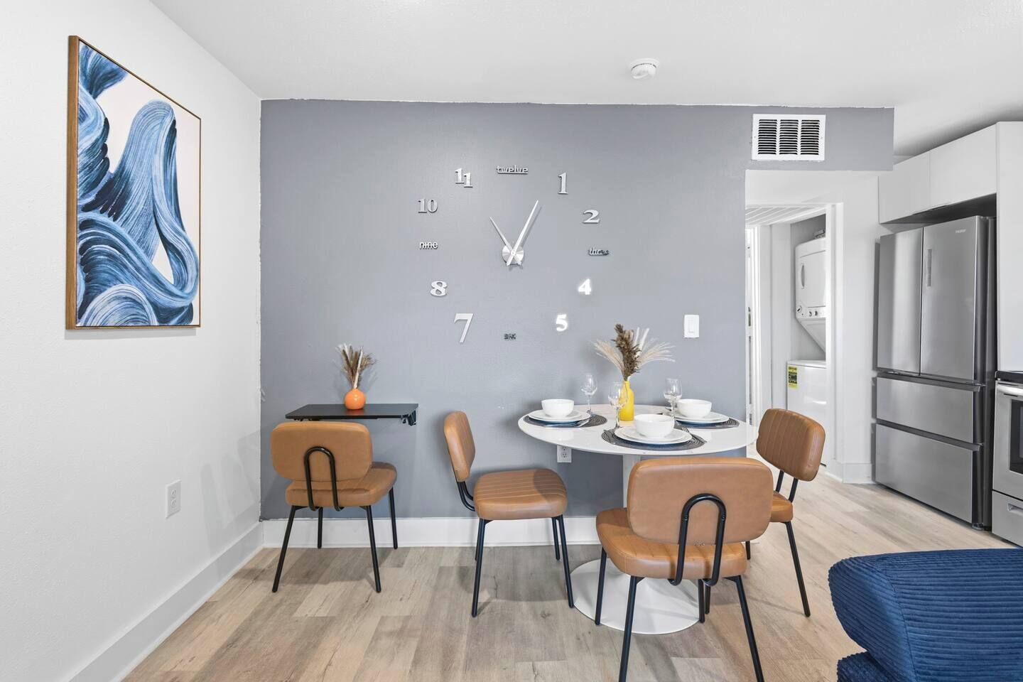 A modern kitchen with a built-in refrigerator, a dining area with a round table and chairs, and a wall clock.