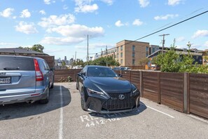 Ein Parkplatz mit zwei Autos, einem Zaun und Gebäuden im Hintergrund.