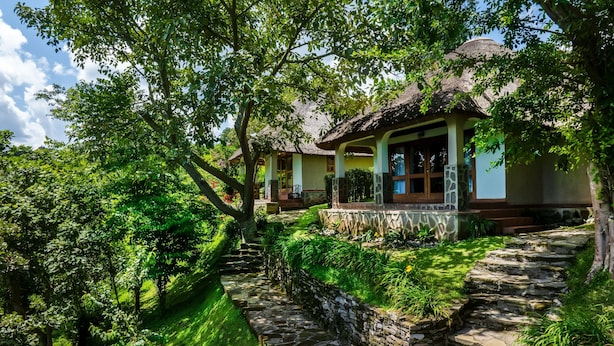 Una casa tradicional amb teulada de palla, envoltada de vegetació exuberante i camins de pedra.