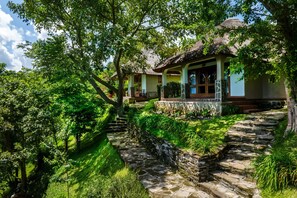 A traditional house with a thatched roof, surrounded by lush greenery and stone pathways. - bahundu Safari Lodge (Fort Portal)